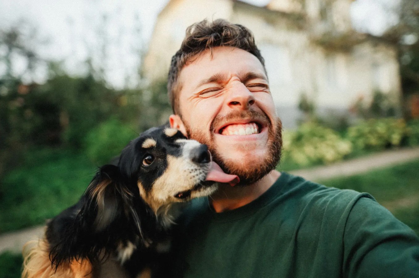 A man smiles for a selfie while his dog playfully licks his face.